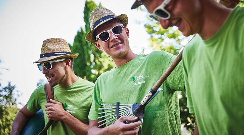 Mitarbeitende eines Gartenbau Betriebs mit Rechen und Werkzeugen in lockerer Stimmung im Arbeitsalltag